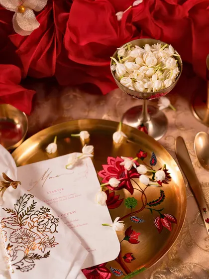 A close-up of the beautiful hand-painted Kalamkari plate from Baarique, paired with a custom menu and fresh jasmine flowers.