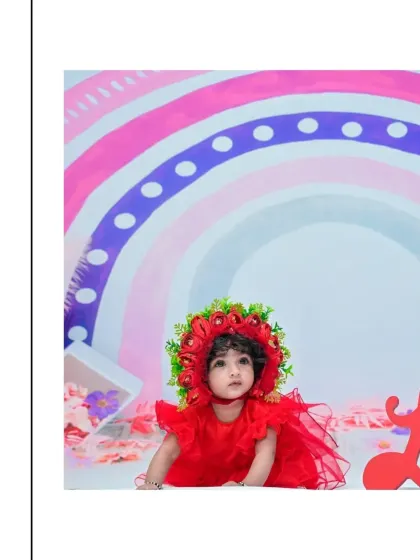 A baby girl in a striking red dress and floral bonnet against a pastel rainbow backdrop. The vibrant colors make for a cheerful and eye-catching portrait.