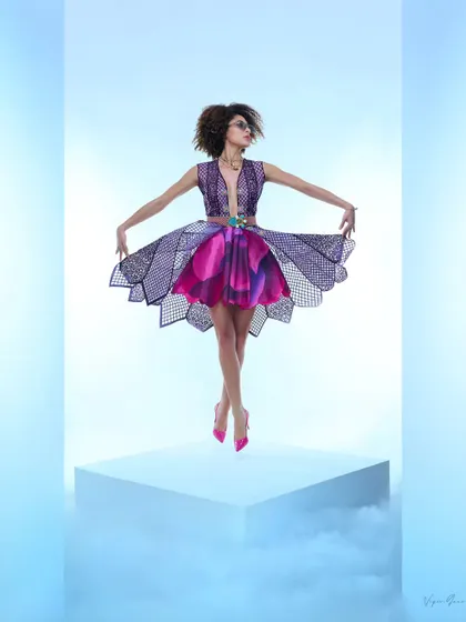 This image from a designer shoot highlights a structured, multi-layered dress. The lighting and pose are designed to showcase the unique cut and vibrant colors of the fabric, creating a visually striking fashion photograph.