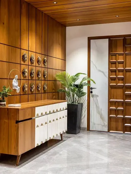 This elegant foyer features a stunning carved wooden door and a console with intricate white detailing. The wall is adorned with decorative brass masks, creating a culturally rich entrance.