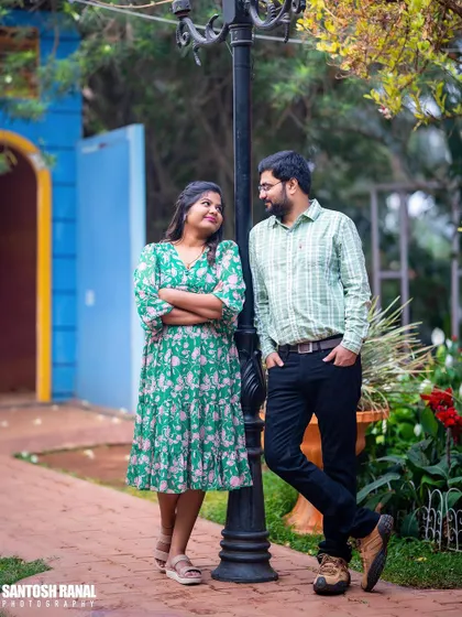A relaxed, stylish portrait of a couple leaning against a lamppost in a garden.