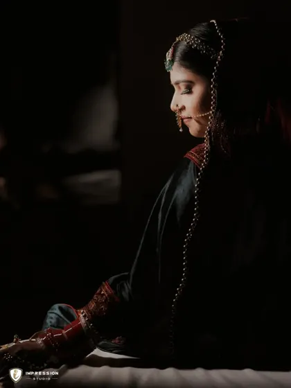 A side profile of the bride in a dark, moody setting, highlighting the silhouette of her face and the details of her attire.