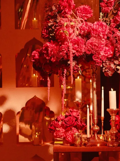 A close-up of a floral centerpiece, with deep red blooms and cascading amaranthus, surrounded by the warm glow of taper candles.