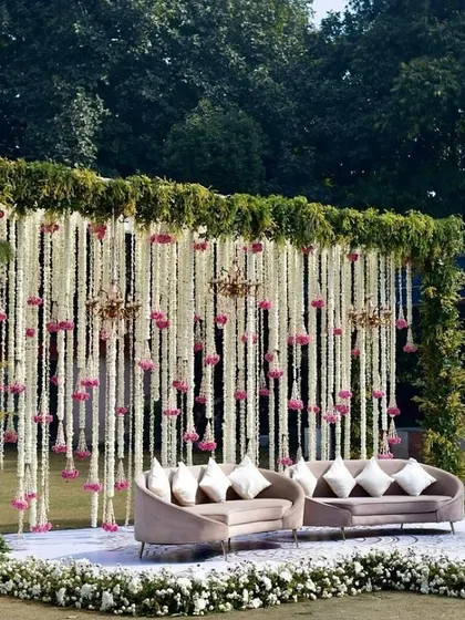 A beautiful outdoor seating area for an evening function. The stage is framed with greenery and features a curtain of hanging white flowers.