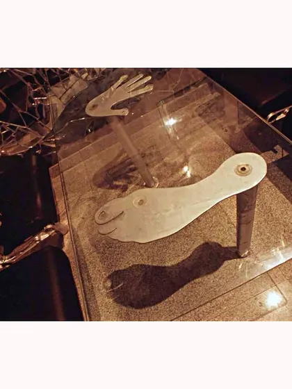 A custom glass table at the Aste Bar features whimsical hand-and-foot-shaped supports. This playful detail adds a touch of humor and artistry to the industrial, upcycled design.