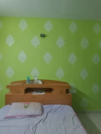 A fresh green bedroom wall decorated with a white damask stencil pattern, adding a touch of classic elegance to the space.