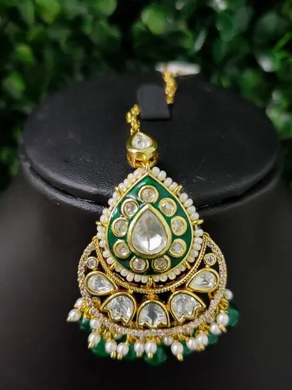 A lovely maang tikka with green enamel work and kundan stones. The green bead drops add a touch of freshness to the design.
