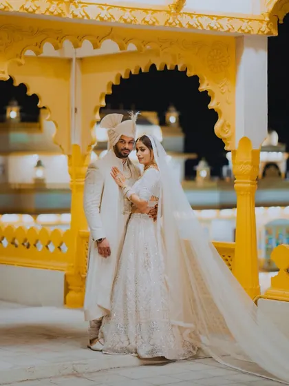 A regal nighttime portrait of the couple against the illuminated architecture of their wedding venue, creating a dramatic and romantic image.