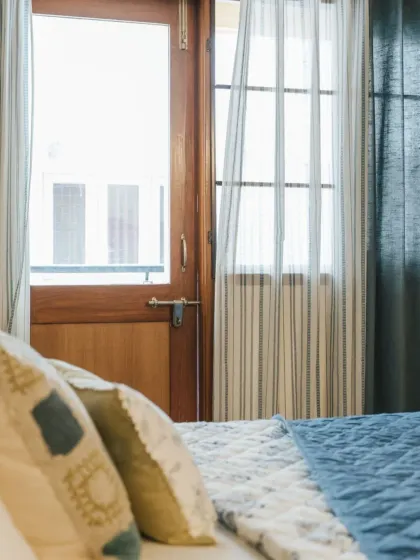 A glimpse into a bedroom we adorned, where our striped sheer curtains and solid drapes frame the view. The mix of cushion patterns on the bed adds texture and completes the cozy, lived-in feel.