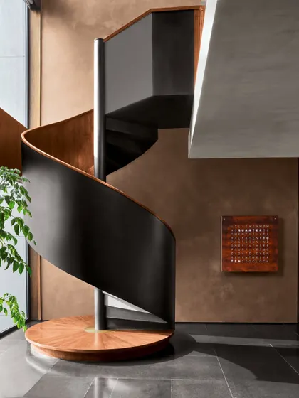 The elegant spiral staircase at the Baid Residence, adorned with a designer clock from Qlocktwo. The warmth of the terracotta paint contrasts beautifully with the sleek, honed black granite flooring.