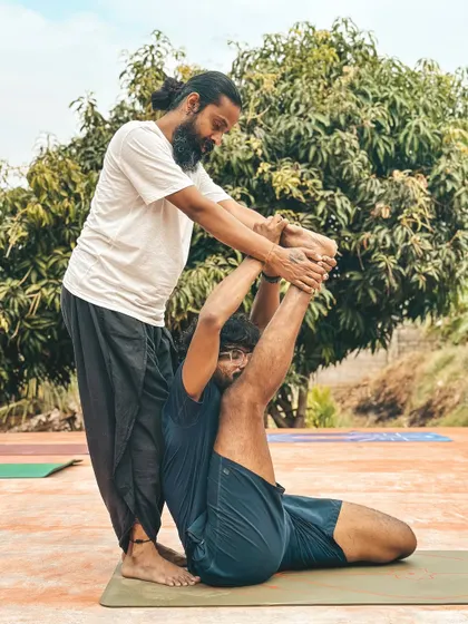 Here, I help a student with Supta Trivikramasana (Reclining Split). This advanced posture requires immense flexibility, and my assistance ensures the student works safely within their range of motion.