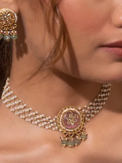 This rice pearl moti choker enhances your elegance with a fusion touch. The multi-strand pearl choker is centered with a pink stone pendant featuring Kundan work, perfectly blending tradition with contemporary style.