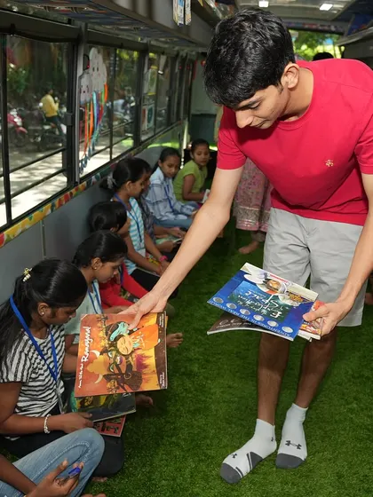 A volunteer from Overbooked.in distributes books to the children inside our mobile library and classroom.