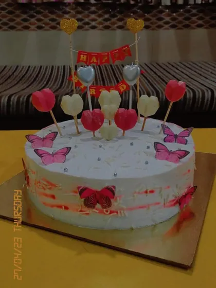 A whimsical and romantic birthday cake. It's decorated with edible butterflies and a variety of heart-shaped lollipops, perfect for a dreamy and sweet celebration.