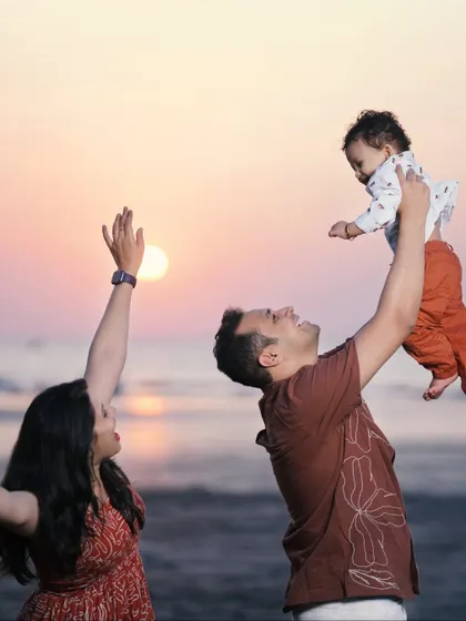 A candid and joyful family photo on the beach at sunset. The action of tossing the baby in the air adds a sense of fun and spontaneity to this beautiful memory.