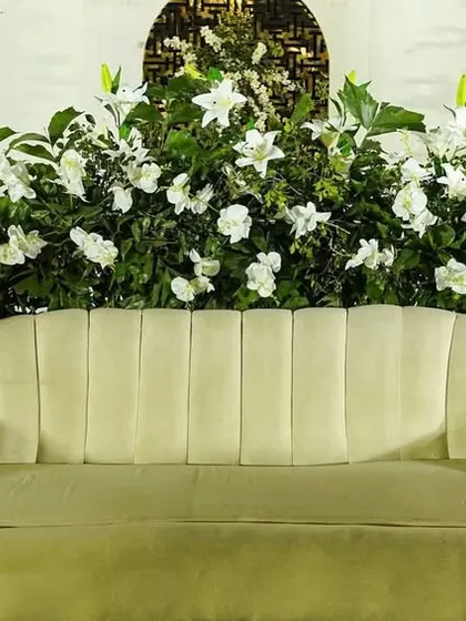 A beautiful backdrop for an engagement or reception, featuring a plush cream-colored sofa surrounded by an abundance of white lilies and other white flowers.