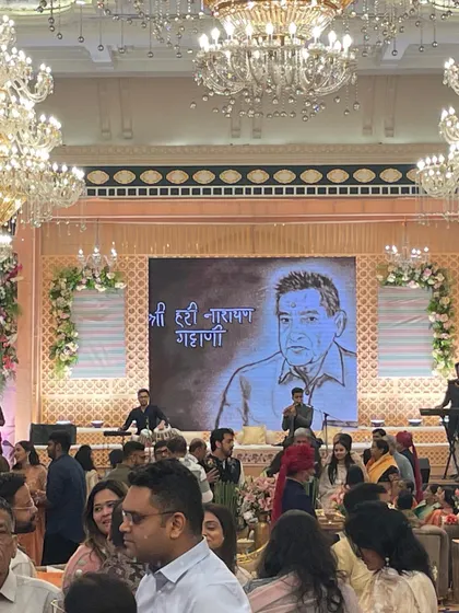 A wide view of the hall during a tribute performance for the Gattani family in Jaipur. The sand art portrait of Shri Hari Narayan Gattani is displayed on the main screen for all guests to see.