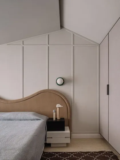 The guest bedroom features a unique design where the headboard and wall paneling become one architectural element. This approach blurs the lines between furniture and structure, creating a cohesive and artful space.