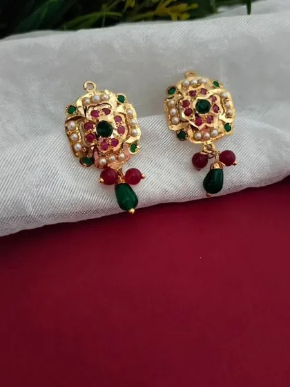A detailed shot of the restocked Jadau pendant set earrings. The design features a floral motif with red and green stones, embodying a classic Indian aesthetic.