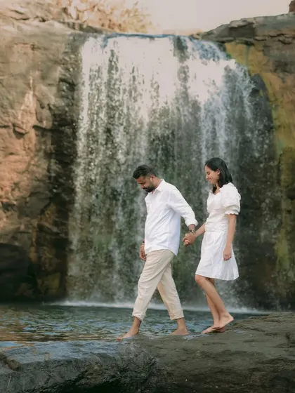 The couple carefully navigating the rocks by the waterfall, symbolizing their support for each other on their new journey.