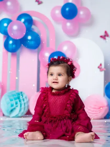 A beautiful portrait of a baby girl in a lovely red dress, surrounded by festive balloons for her first birthday.