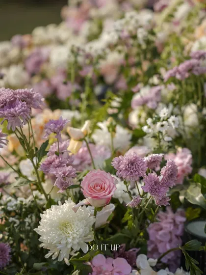A close-up of a garden-style arrangement, with a mix of pink roses, white chrysanthemums, and purple asters. The composition feels natural, as if it were a small piece of a wild meadow.