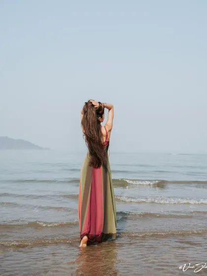Facing the open sea, this shot creates a sense of wonder and scale. The model's long hair and flowing dress interact with the environment, making the image feel alive.