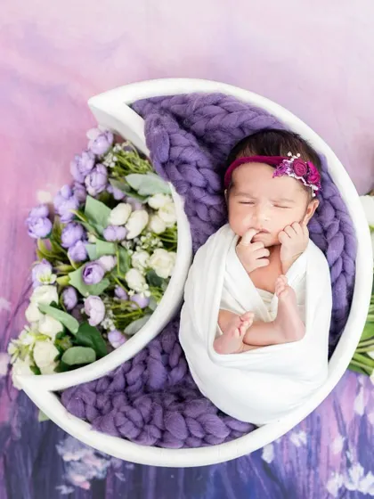 A peacefully sleeping newborn nestled in a celestial moon prop, surrounded by delicate purple and white flowers. This image showcases one of our many creative and safe newborn photography themes.