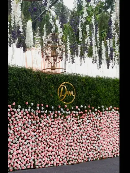 This reception stage features a custom monogram and a two-toned flower wall with pink roses at the bottom and a green hedge on top. I added a hanging birdcage chandelier and white floral strings for a whimsical touch.