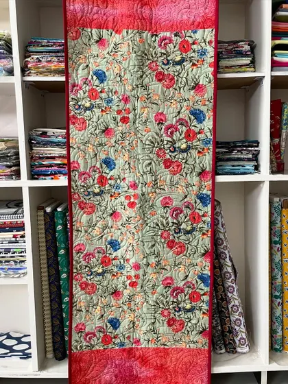 A long table runner featuring a beautiful floral print and solid red ends.