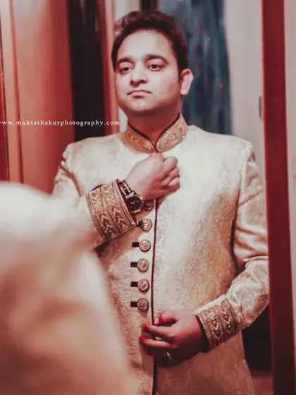 Adjusting the collar of his sherwani, the groom prepares for the main event. These getting-ready photos build the narrative of the day.