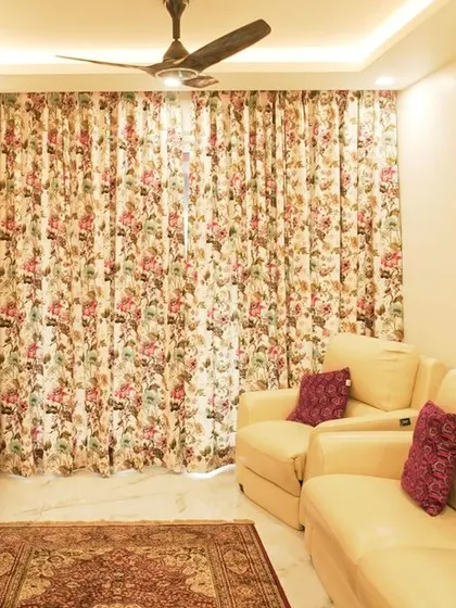 A living room with a large floral curtain as a backdrop. The TV unit is simple and functional, allowing the bold pattern of the curtains to be the main feature.
