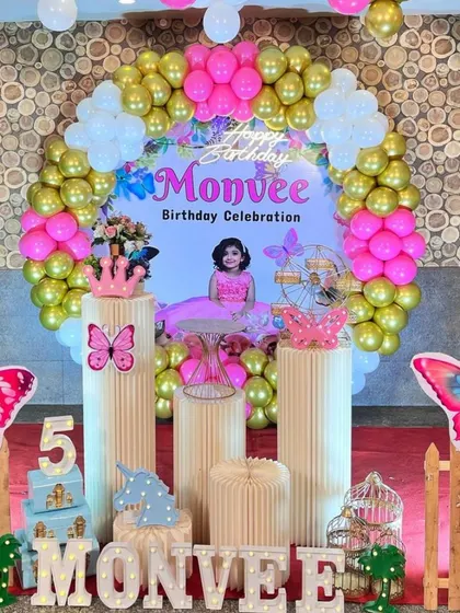 A vibrant butterfly theme for a fifth birthday. This setup features a circular backdrop with a photo, large butterfly cutouts, and a pink and gold balloon arch.