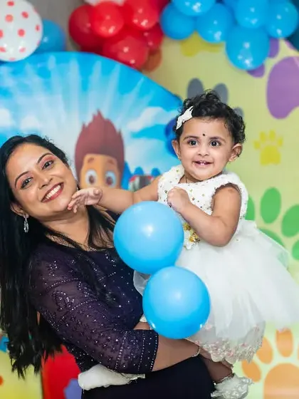 A happy mother and her one-year-old daughter enjoying the party. The colorful decorations and the birthday girl's smile make this a bright and cheerful photograph.