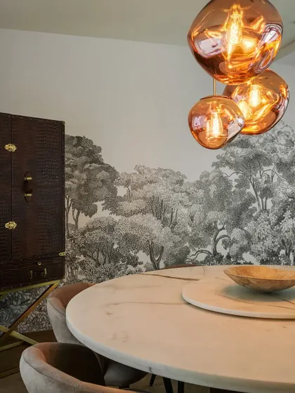 This moody and dramatic dining space features a black and white forest mural and striking copper-toned pendant lights. The round marble table adds a touch of luxe to the intimate setting.