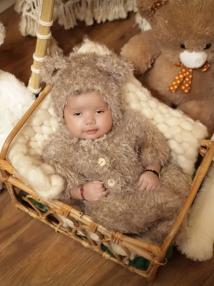 A baby dressed in a fluffy bear costume is surrounded by teddy bears. This overhead shot is a whimsical and creative way to capture a milestone session.