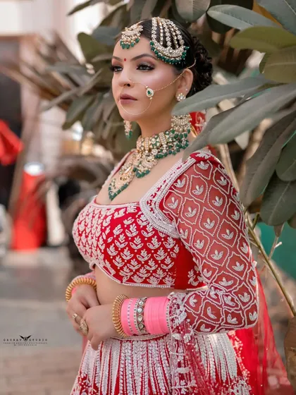 A three-quarter portrait of the bride looking away from the camera. The natural background complements her red and white lehenga, creating a fresh and vibrant image.