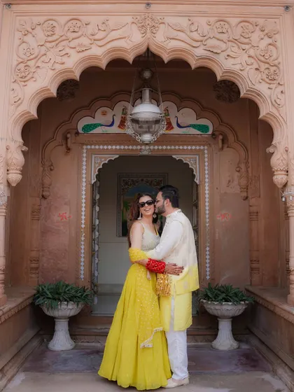 A sweet moment with the groom kissing the bride's cheek against the backdrop of a grand palace door, their yellow outfits vibrant and joyful.