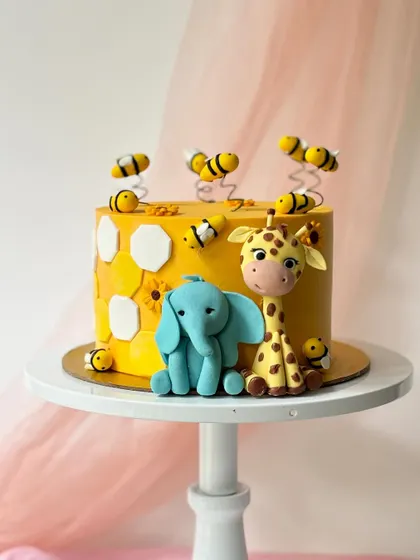 A unique animal-themed cake with a buzzing bee twist. This yellow cake features an elephant and giraffe surrounded by cute, bouncy fondant bees and a honeycomb pattern.