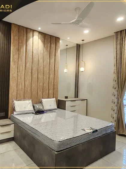 A modern bedroom with a two-tone upholstered headboard in dark wood and beige fabric. The design includes sleek, handleless side tables and elegant pendant lights.