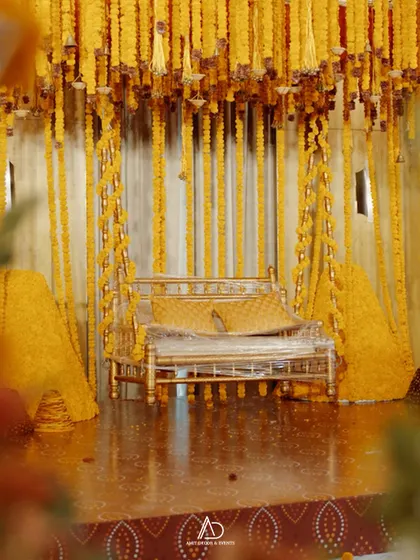 A traditional swing (jhoola) decorated with a dense canopy of marigold strings, set on a reflective floor for a stunning visual effect.