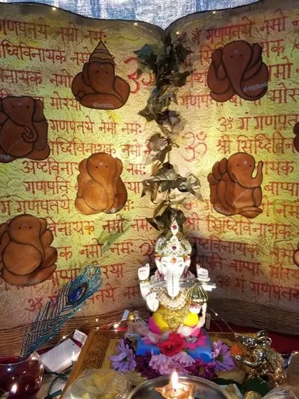 A creative and traditional Ganpati decoration featuring a backdrop designed like an open holy book. The page displays mantras and illustrations of the Ashtavinayak, creating a deeply spiritual setting for the idol.