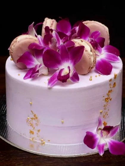This tropical-themed pineapple cake is decorated with fresh purple orchids and macarons. The light purple buttercream and flecks of gold leaf give it a simple yet sophisticated feel.