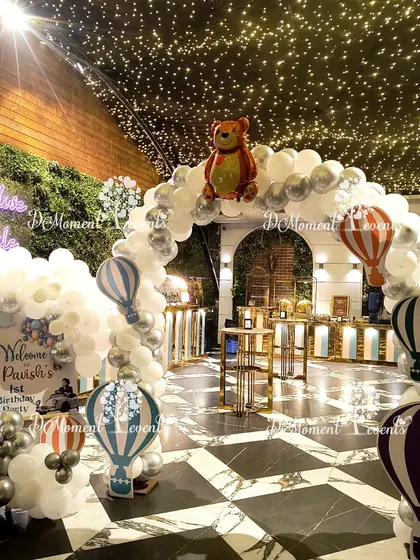 The entrance to the celestial-themed party, with a white balloon arch decorated with hot air balloon cutouts under a ceiling of fairy lights.