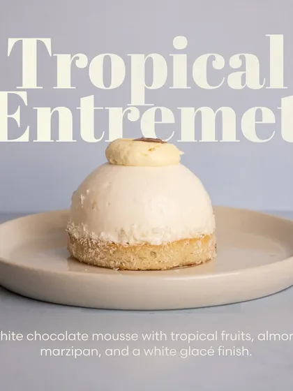 A still shot of the elegant Tropical Entremet, highlighting its smooth white glacé finish and delicate fruit filling.