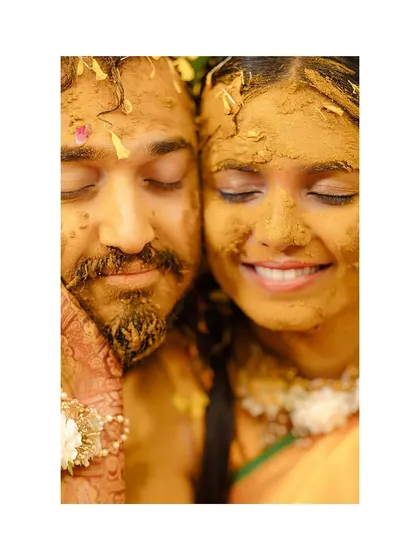 A beautiful, serene close-up of the couple with their eyes closed, faces covered in Haldi, soaking in the moment.