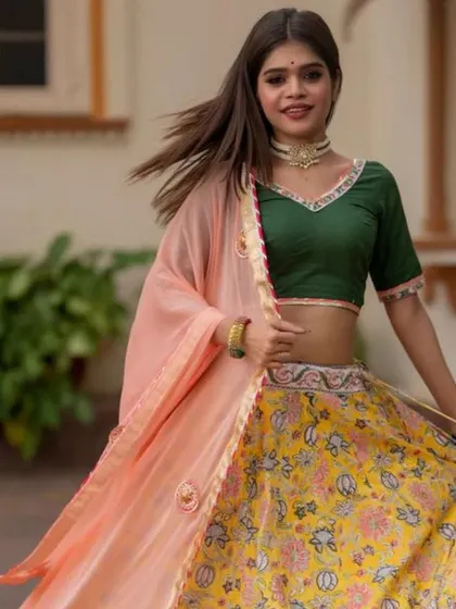 A model in a yellow and green lehenga twirls, showcasing a simple choker necklace that completes her festive look.