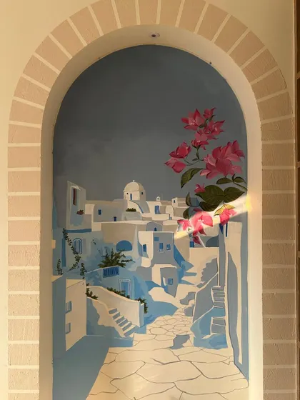 Adding the final touches of bougainvillea to the Santorini mural. The bright pink flowers bring life and vibrancy to the serene blue and white cityscape.