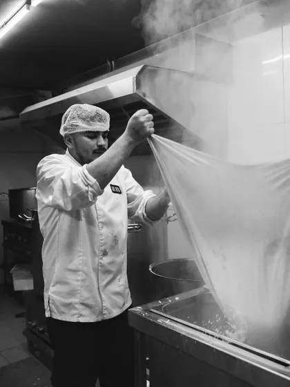 A black and white shot of our cheesemaker at work, straining the curds. It captures the timeless, artisanal nature of our craft.