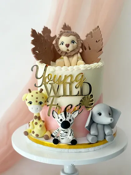 A "Young, Wild & Three" safari cake. This design features a lion, zebra, giraffe, and elephant, with a mix of fondant and paper leaves for texture.